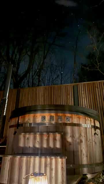 Romantický glamping — siluety sauny a hutky proti tmavomodrému nebi s girlandami světel