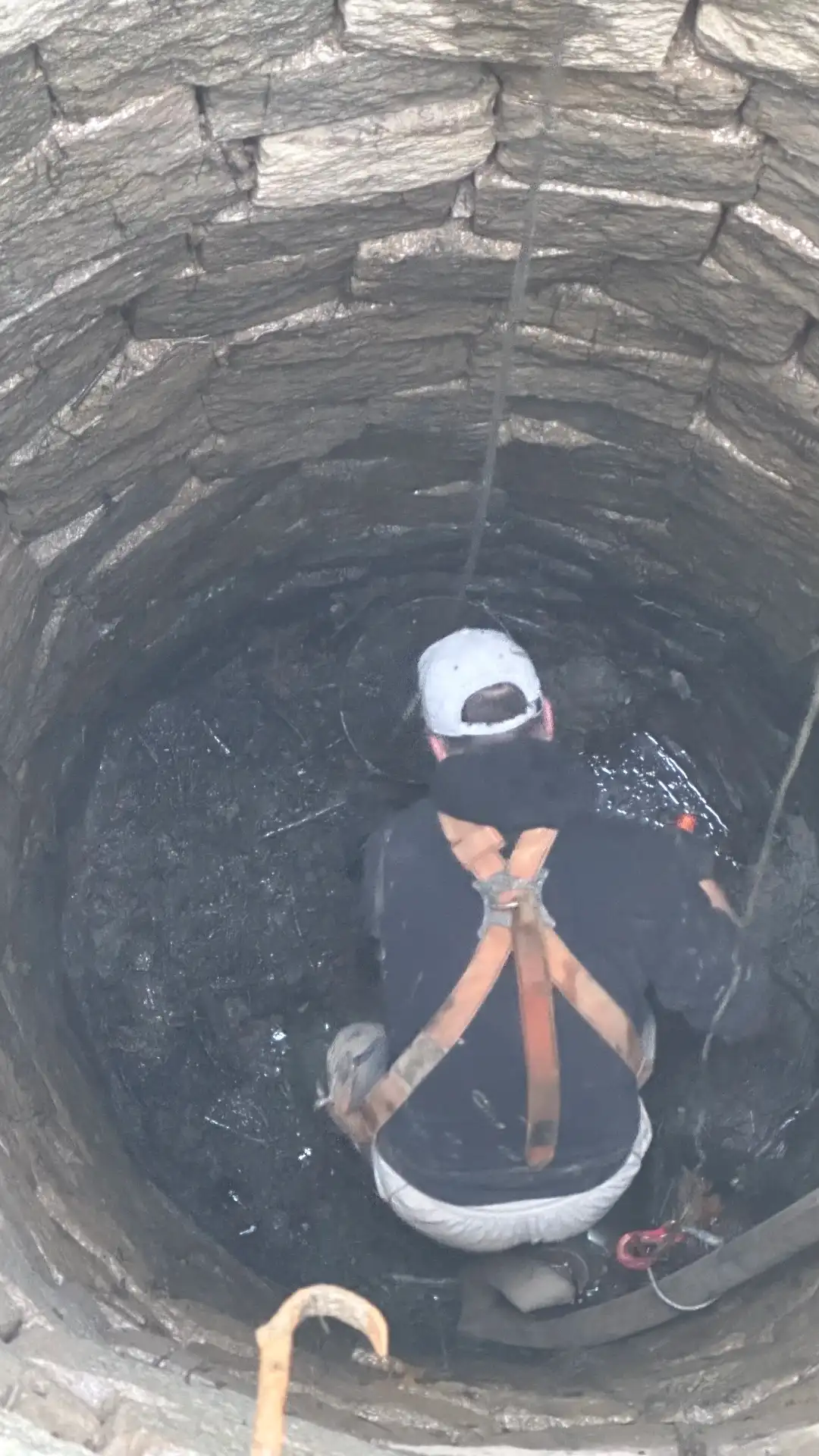 View from above into the well during cleaning — stone masonry, person at the bottom in a harness